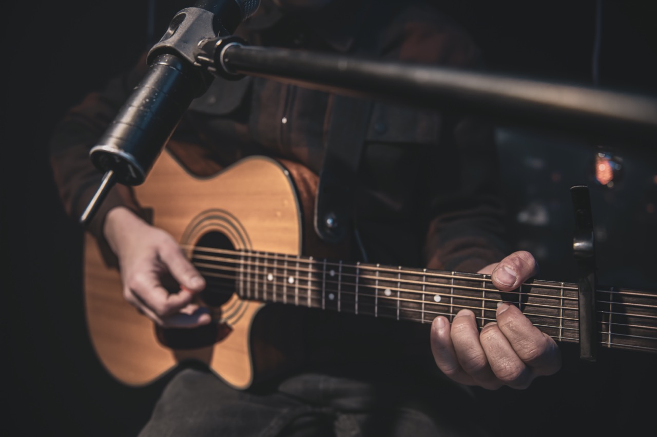 The guitarist plays an acoustic guitar with a capo in front of a microphone. The concept of music recording, rehearsal or live performance.
